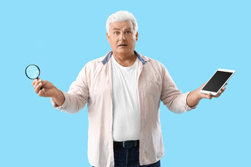 Confused senior man with magnifier and tablet computer on blue background