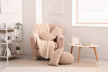 Cozy armchair with cushions and blanket in interior of light living room