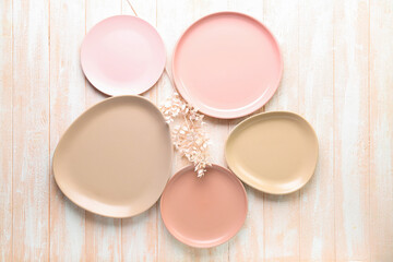 Clean ceramic plates and floral decor on pink wooden background