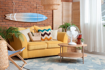 Interior of stylish living room with yellow sofa, surfing board and electric fan on coffee table