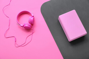 Yoga mat with foam exercise block and headphones on pink background