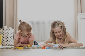 Naklejka premium Children playing with colorful toys. Kids sitting on carpet at home bedroom or kindergarten. Development of fine motor skills, imagination, logical thinking concept. Educational eco-friendly games