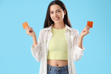 Young woman with condoms on blue background - obrazy, fototapety, plakaty