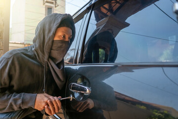 Car thief in mask tries to open car door with screwdriver. The thief tries to break the car window...