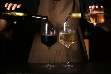 Female bartender pouring different wine from bottles into glasses on table in bar