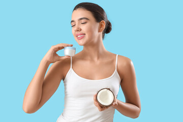 Pretty young woman with cream and coconut on blue background