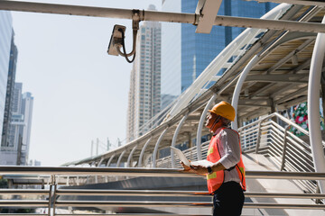 Caucasian man technician or engineer using laptop computer check work fixing video surveillance camera CCTV. Professional doing a preventive maintenance, inspection security camera on city background.