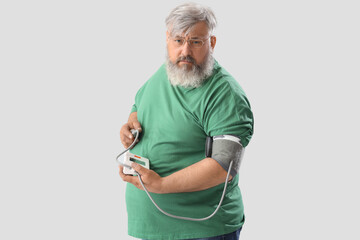 Senior man measuring his blood pressure on light background