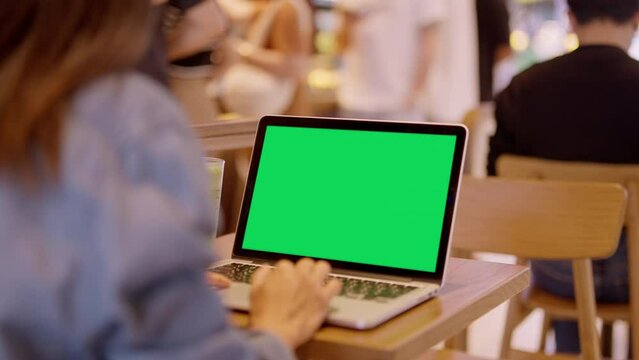 Over the shoulder shot of woman, using finger with keyboard for typing touch. computer laptop with blank green screen chroma key in cafe.