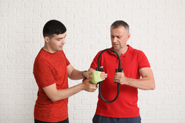 Mature man training with pilates circle and rehabilitation therapist on white brick background