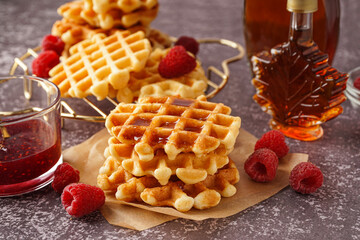 Tasty waffles with raspberries and maple syrup on grey background