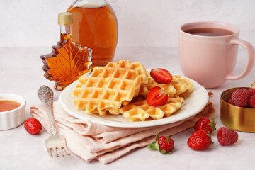 Tasty waffles with berries, maple syrup and cup of tea on white background