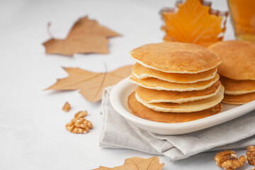 Plate of tasty pancakes with nuts and maple syrup on white background