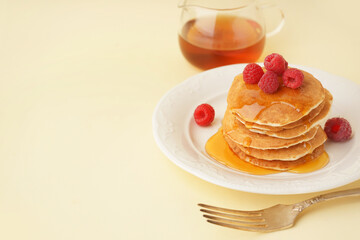 Plate of tasty pancakes with raspberries and maple syrup on yellow background