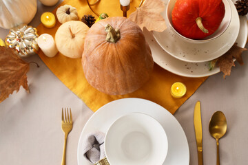 Elegant table setting with clean dishes, golden cutlery and pumpkins for Halloween party