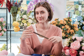 Fototapeta premium A young White Asian female florist entrepreneur blossoms arranging, decorating, happy work in colorful flower shop store with blooms, and small business owner.