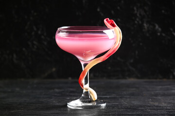 Glass of delicious pink cocktail and candy for Halloween celebration on black background