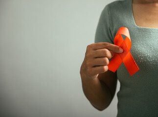 Studio shot of a woman in uniform holding an HIV AIDS awareness red ribbon on her chest. Isolated...