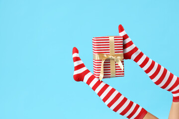 Young woman in Christmas stockings with gift on blue background
