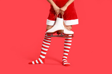 Young woman in Christmas stockings with ice skates on red background