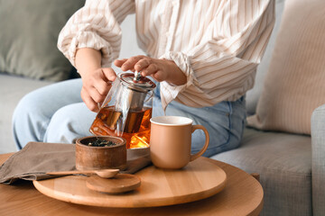 Young woman pouring hot tea into cup at home, closeup