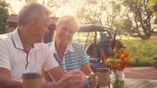 Senior retired couple sitting having coffee after round of golf looking at score card together - shot in slow motion
