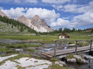 Fototapeta na wymiar Small Wooden Bridge, Wooden Hut and Le Vert Lake in the Greenery of the Fanes - Senes - Braies Nature Park, Alps Mountains, Italy