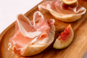 Wooden board with of tasty sandwiches with prosciutto on white background
