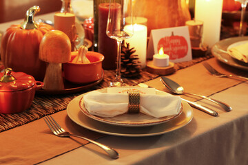 Festive table setting with burning candles, pumpkins and folded napkin for Thanksgiving dinner, closeup