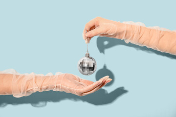 Female hands holding silver Christmas ball on blue background