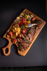 fried pieces of steak with vegetables on the grill on a wooden tray
