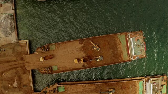 Dump trucks and excavators loading nickel ore onto barges at a sumitomo mining site in Taganito Philippines.