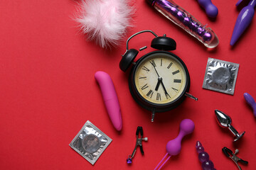 Alarm clock with different toys and condoms on red background. Time for sex