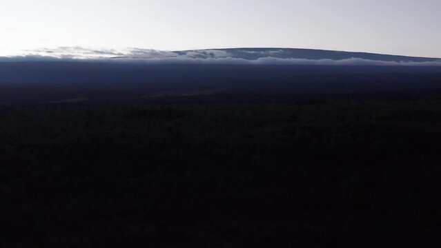 Aerial wide rising shot of the volcano Mauna Loa revealed above the clouds at sunset on the Big Island of Hawai'i. 4K