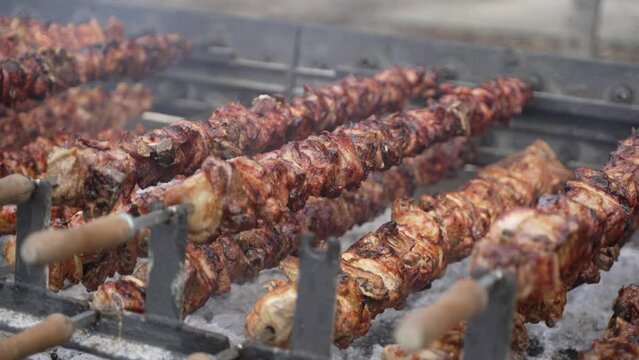 Close-up pork and chicken skewers rotating on a spit over hot coals.