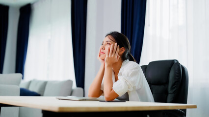 Bored young asian woman sitting at her workplace at home, boring expression is thinking of something