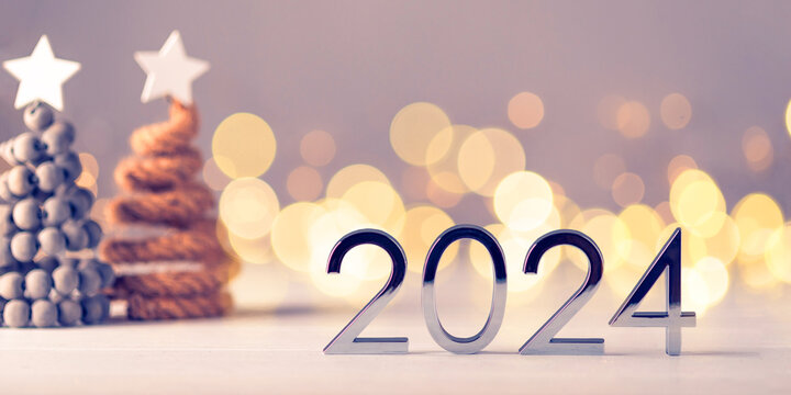 Metal numbers 2024 on a white table with Christmas trees and bokeh lights. Happy New Year 2024 is coming concept.