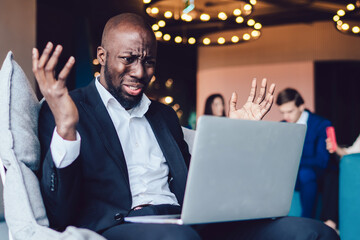 Disappointed African American office worker having problem with laptop at lobby of business center