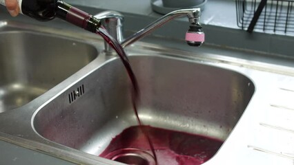 An alcoholic pouring away wine from a bottle down the drain of a sink giving up and overcoming alcohol addiction