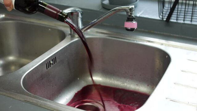 An alcoholic pouring away wine from a bottle down the drain of a sink giving up and overcoming alcohol addiction