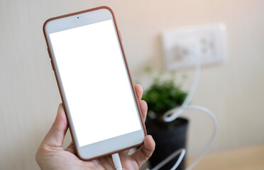 Charging a smartphone via a USB cable on woman hand. Close up of a white smartphone with a white blank screen.