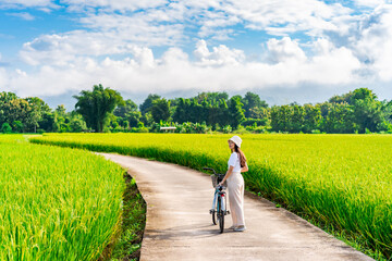 Young happy woman tourist enjoying and riding a bicycle in paddy field while traveling at Nan, Thailand - obrazy, fototapety, plakaty