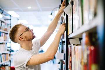 Thoughtful student searching book on bookshelf in library