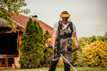 Senior man, equipped in safety gear, skillfully using a grass trimmer to maintain his lush green lawn in his retirement oasis
