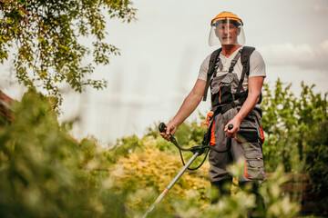 A seasoned gardener, dressed in a protective work suit, meticulously trimming the edges of his well-kept garden with a grass trimmer