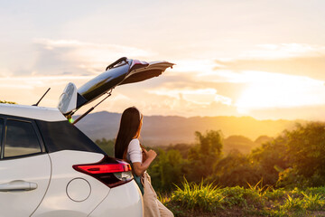 Young woman traveler with car watching a beautiful sunrise over the mountain while traveling road trip on vacation, Travel concept - obrazy, fototapety, plakaty