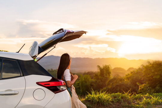 Young woman traveler with car watching a beautiful sunrise over the mountain while traveling road trip on vacation, Travel concept