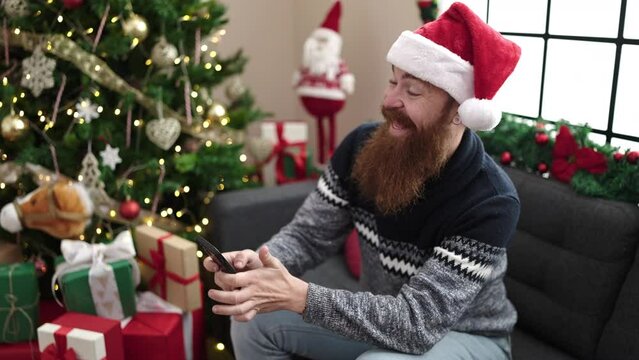 Young redhead man make selfie by smartphone sitting on sofa by christmas tree at home