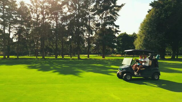 Drone shot of senior retired couple riding in golf buggy on course- shot in slow motion