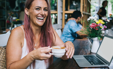 Excited lady with cup of coffee and laptop in cafe